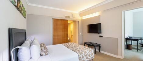 A hotel room with a bed, bedside table, TV, and a desk with a chair.