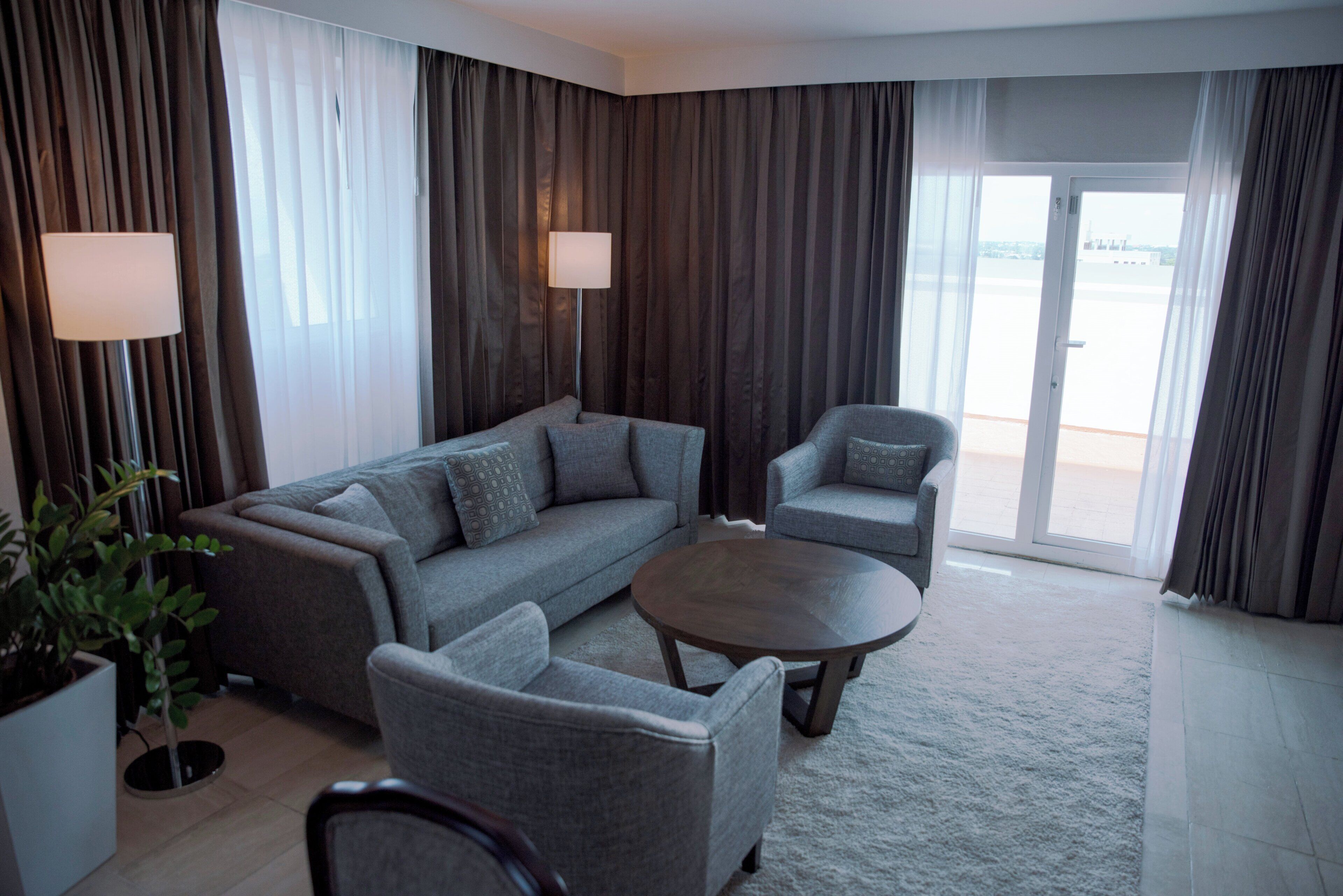 A modern living room with a sofa, armchair, and coffee table. There is a potted plant and a lamp.