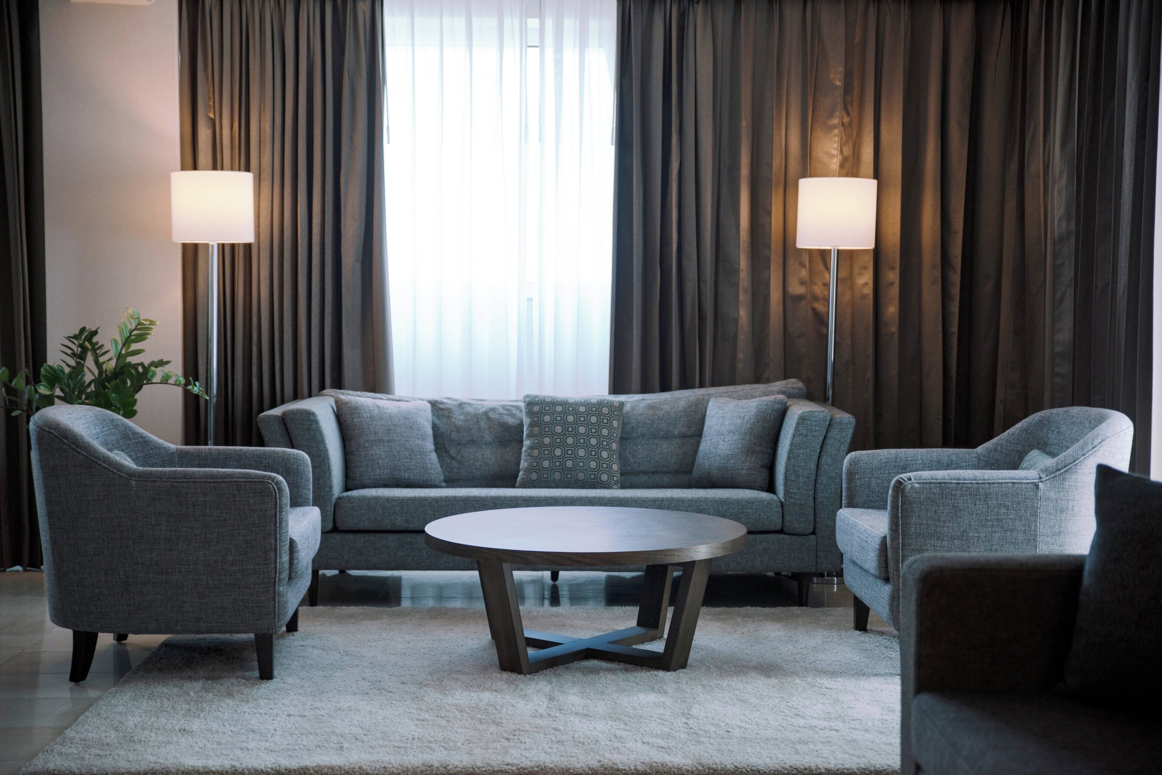 A modern living room with a grey sofa, two armchairs, a round coffee table, and a potted plant.