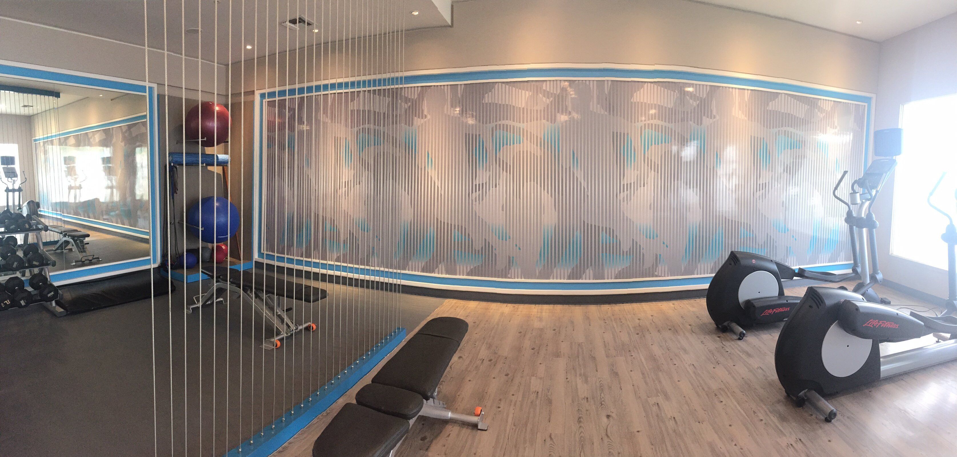 A gym with exercise equipment, a mirrored wall, and a wooden floor.