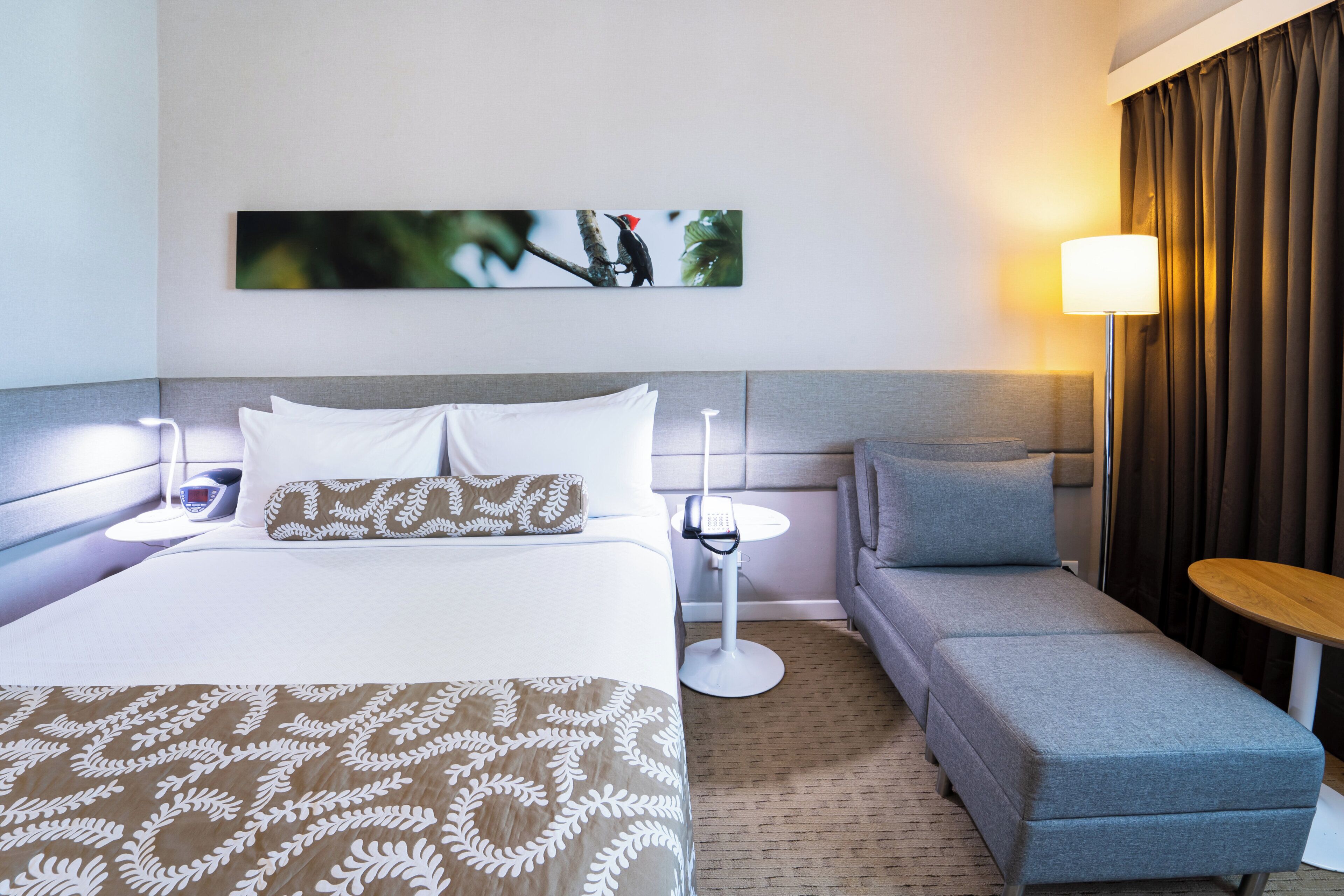Ein Hotelzimmer mit Bett, Sofa, kleinem Tisch, Lampe und einem Bild an der Wand.