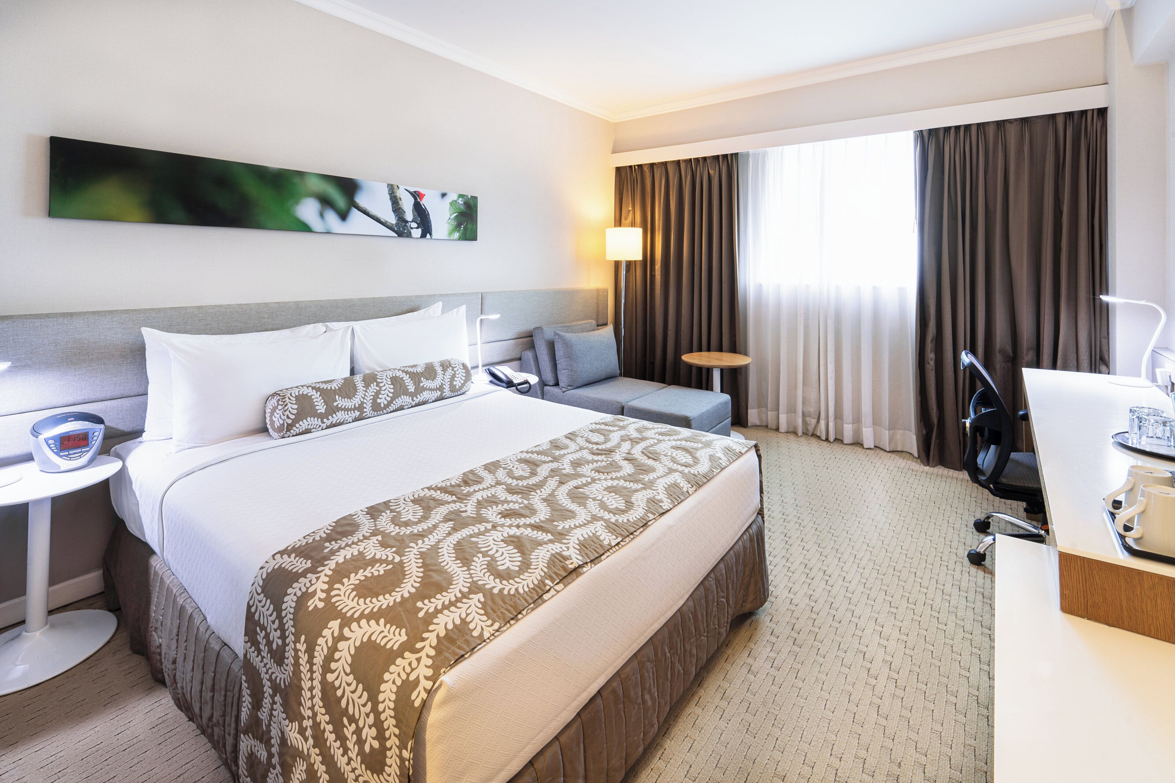 A hotel room with a large bed, a desk with a chair, a small table, and a lamp.