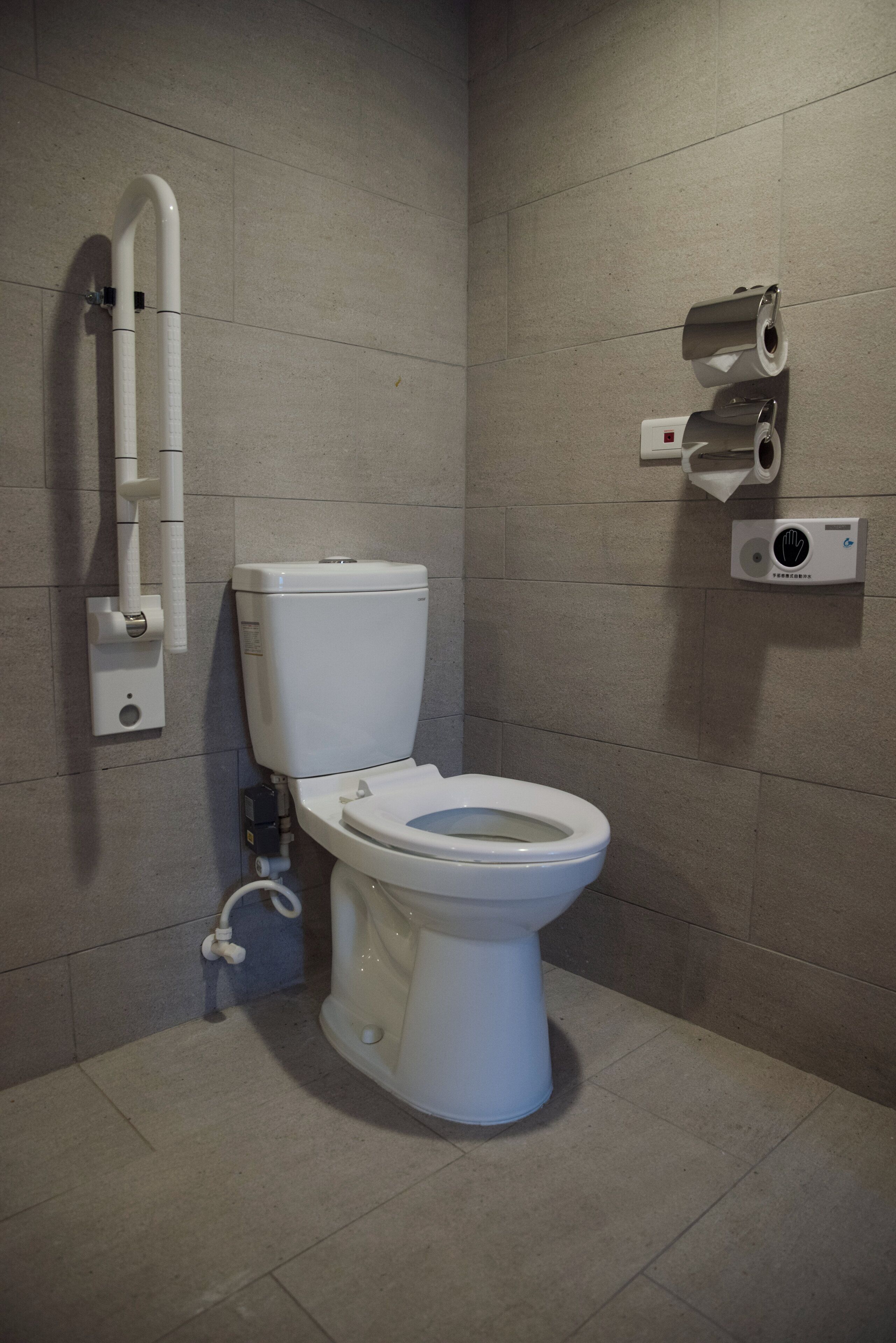 A modern bathroom with a white toilet, a hand sanitizer dispenser, and a toilet paper holder on the wall.