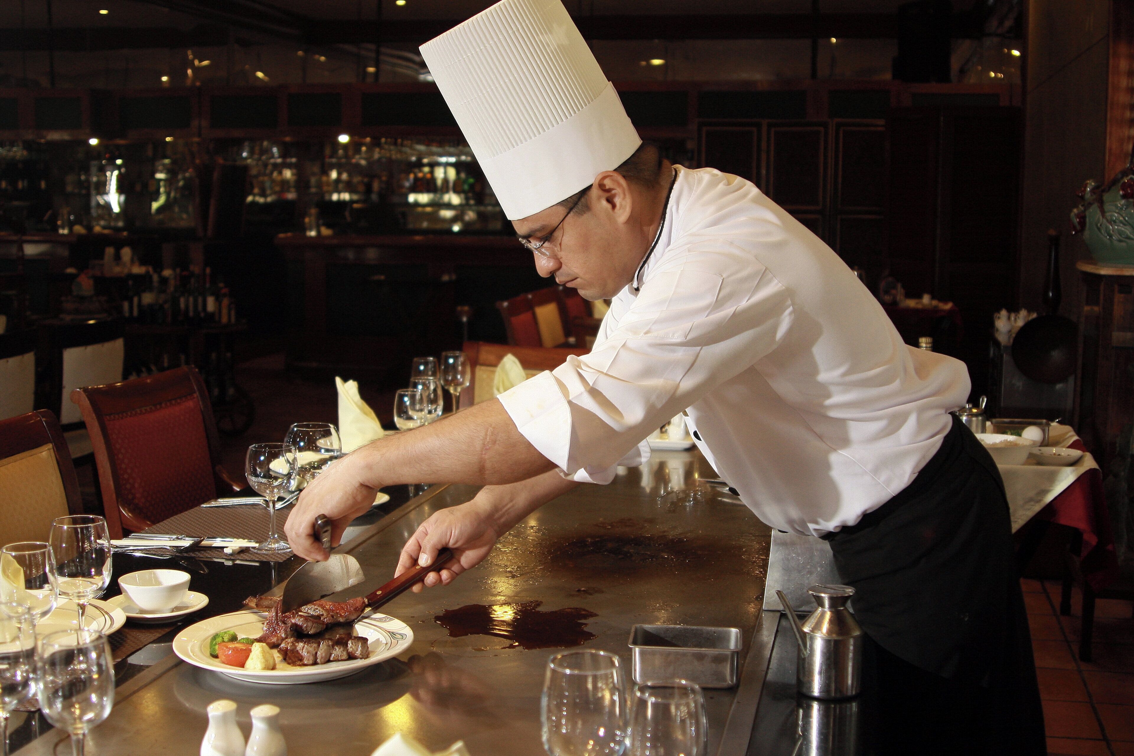 A chef preparing food at a restaurant table with various dishes and utensils.
