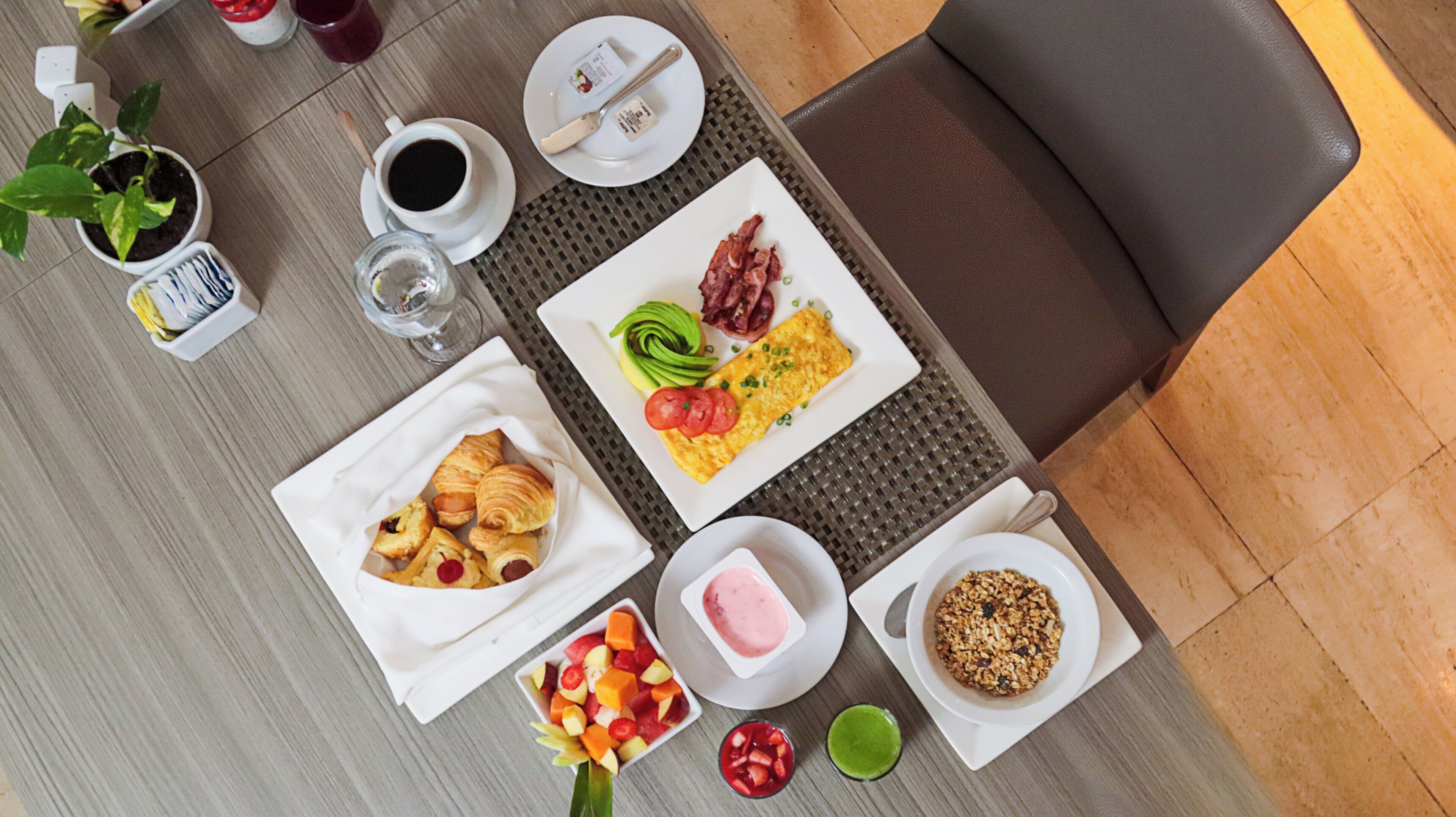 A breakfast table with croissants, fruit, eggs, bacon, and a beverage.