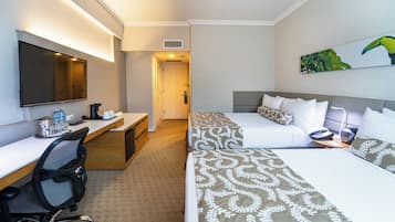 Habitación de hotel con escritorio, dos camas, una silla, televisor y un cuadro.