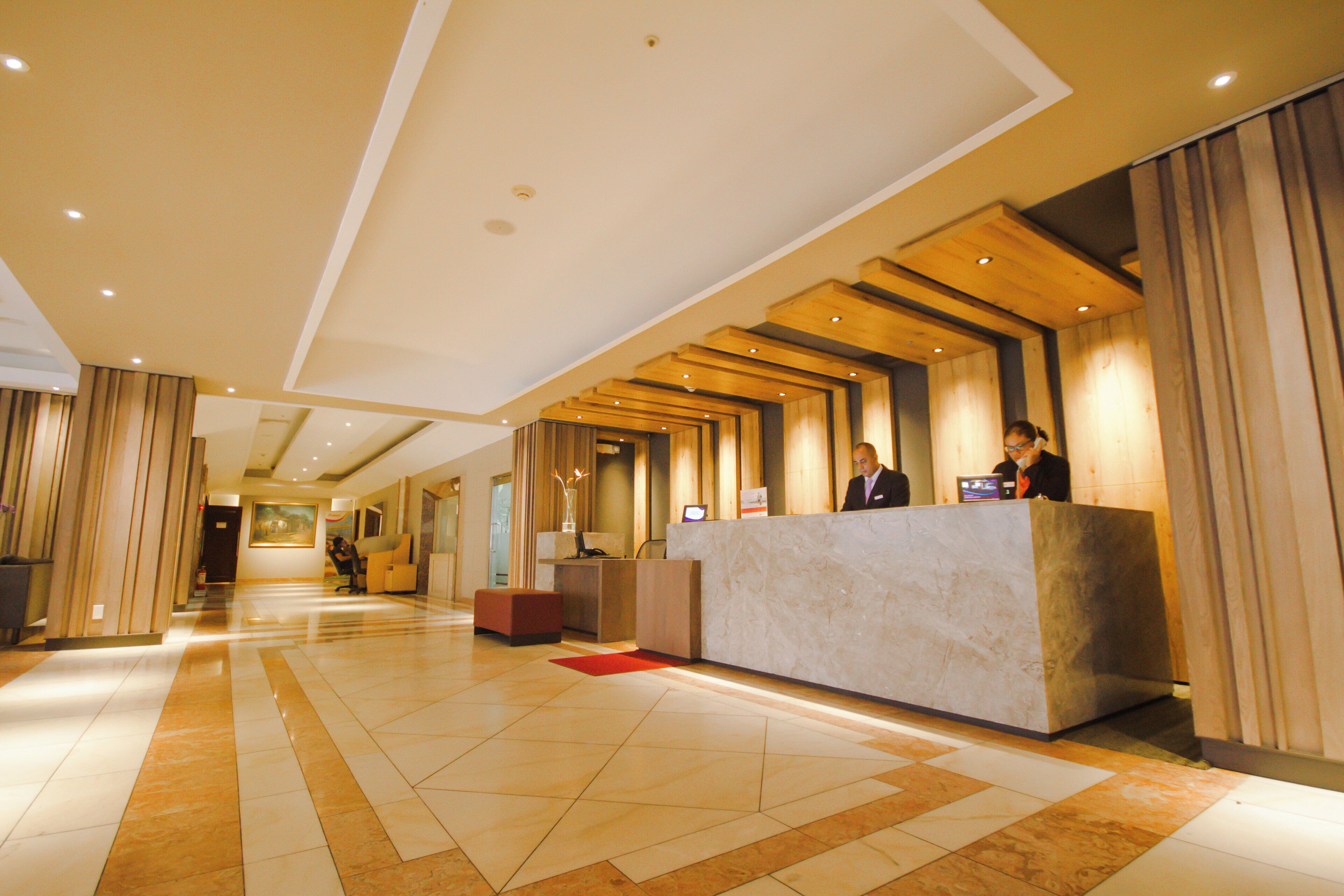 A hotel reception area with a marble reception desk, wooden paneling on the walls, and a tiled floor.