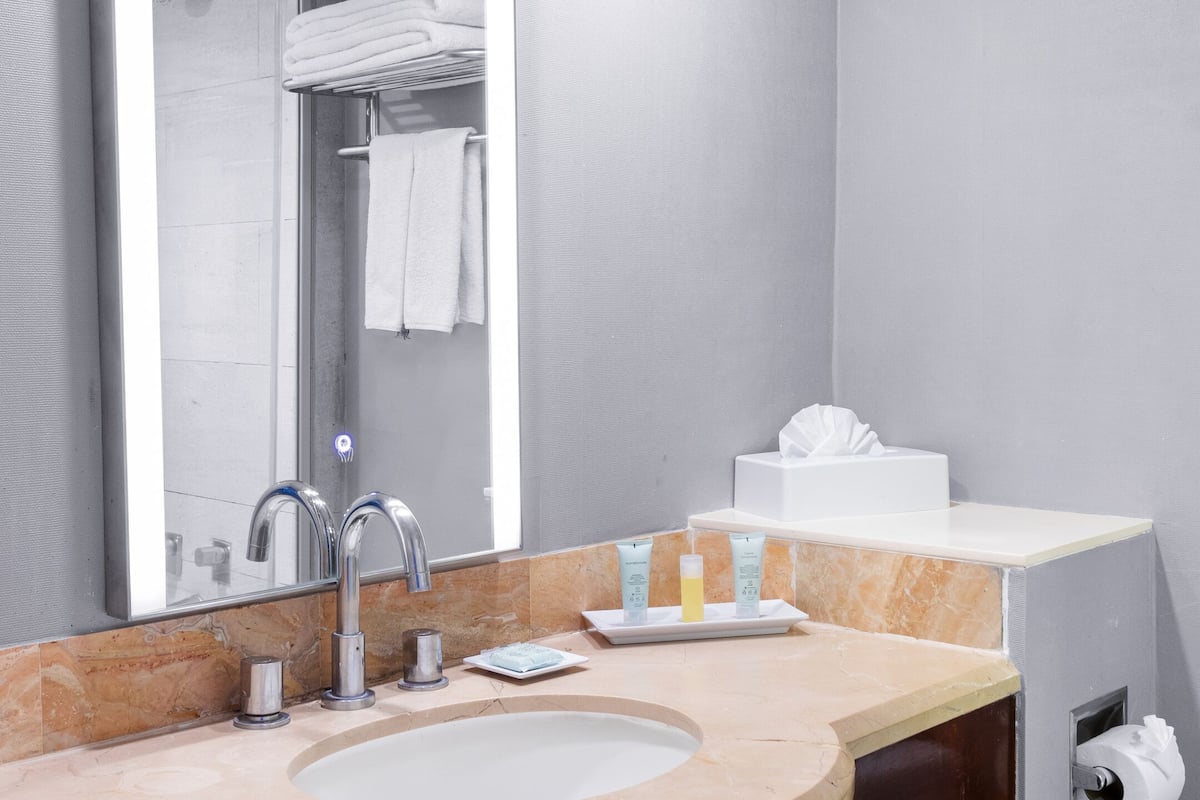 Un bagno moderno con uno specchio grande, un lavabo con piano in marmo e una doccia visibile nel riflesso.