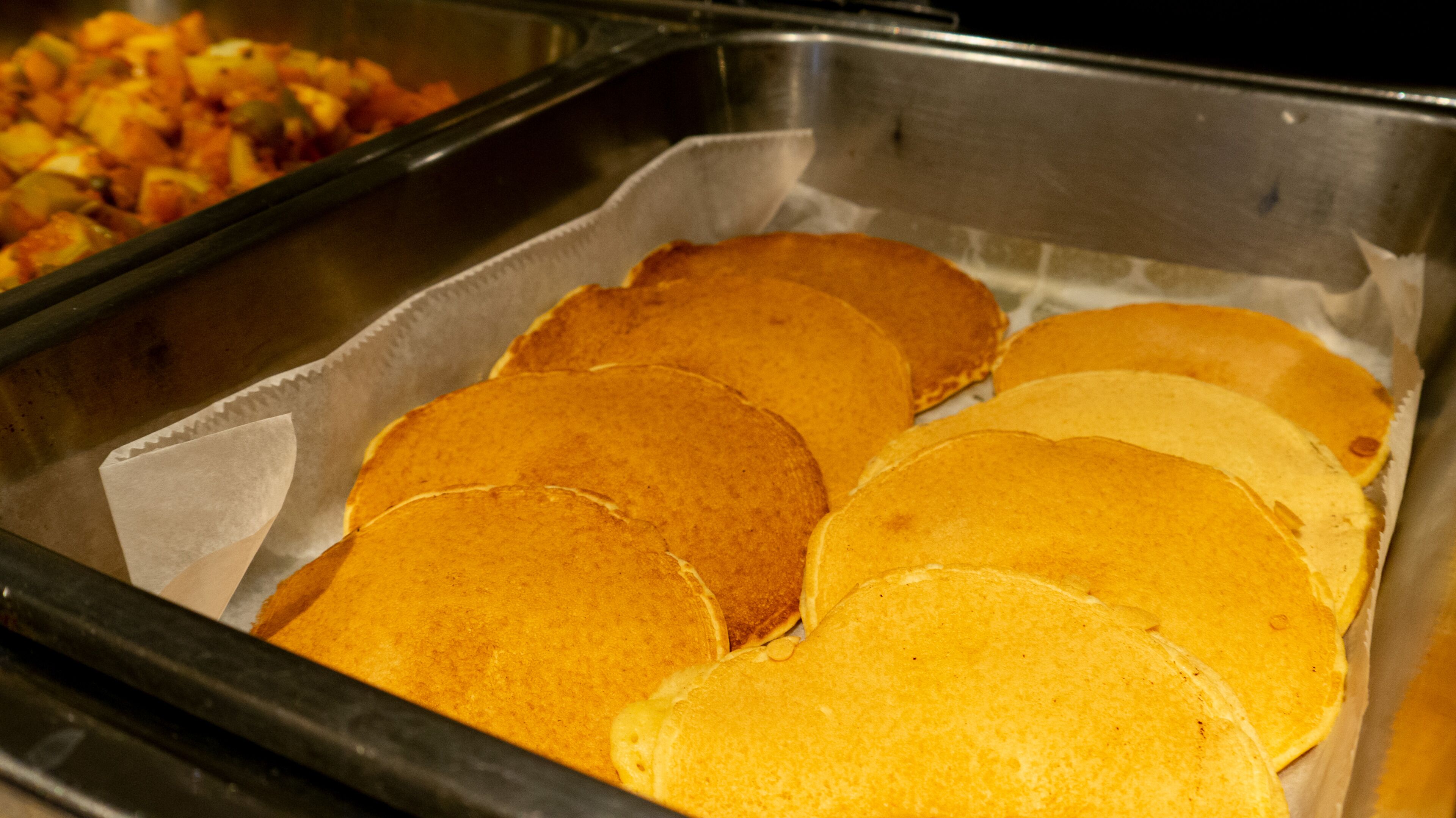 A buffet with several pancakes and a dish of mixed vegetables.