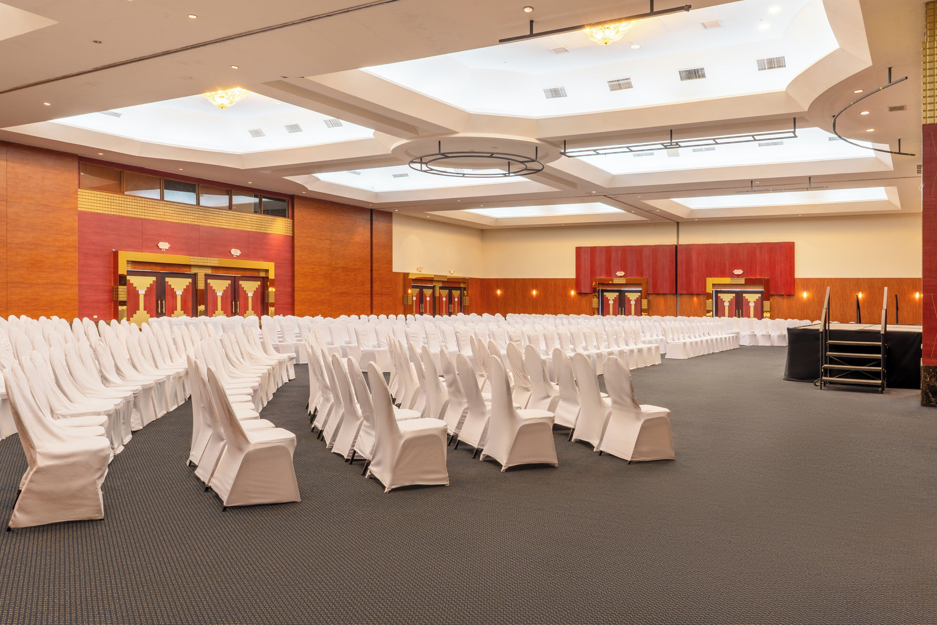 A large conference room with rows of white chairs, a high ceiling with skylights, and a carpeted floor.