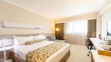A hotel room with a bed, bedside tables, a desk, a chair, a lamp, a television, and curtains.