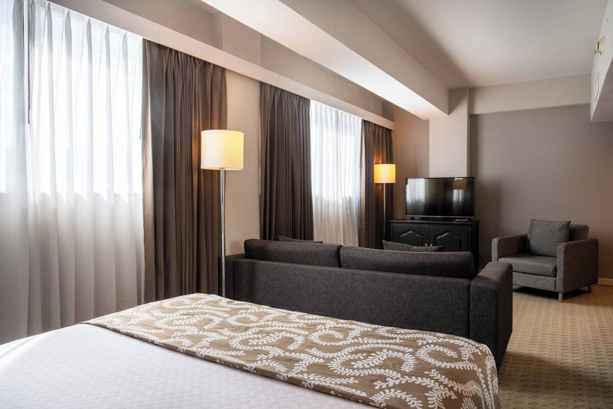 A hotel room with a bed, two armchairs, a television, and a minibar.