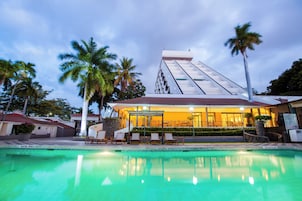 A hotel with a swimming pool, palm trees, and a modern building with a sloped roof.