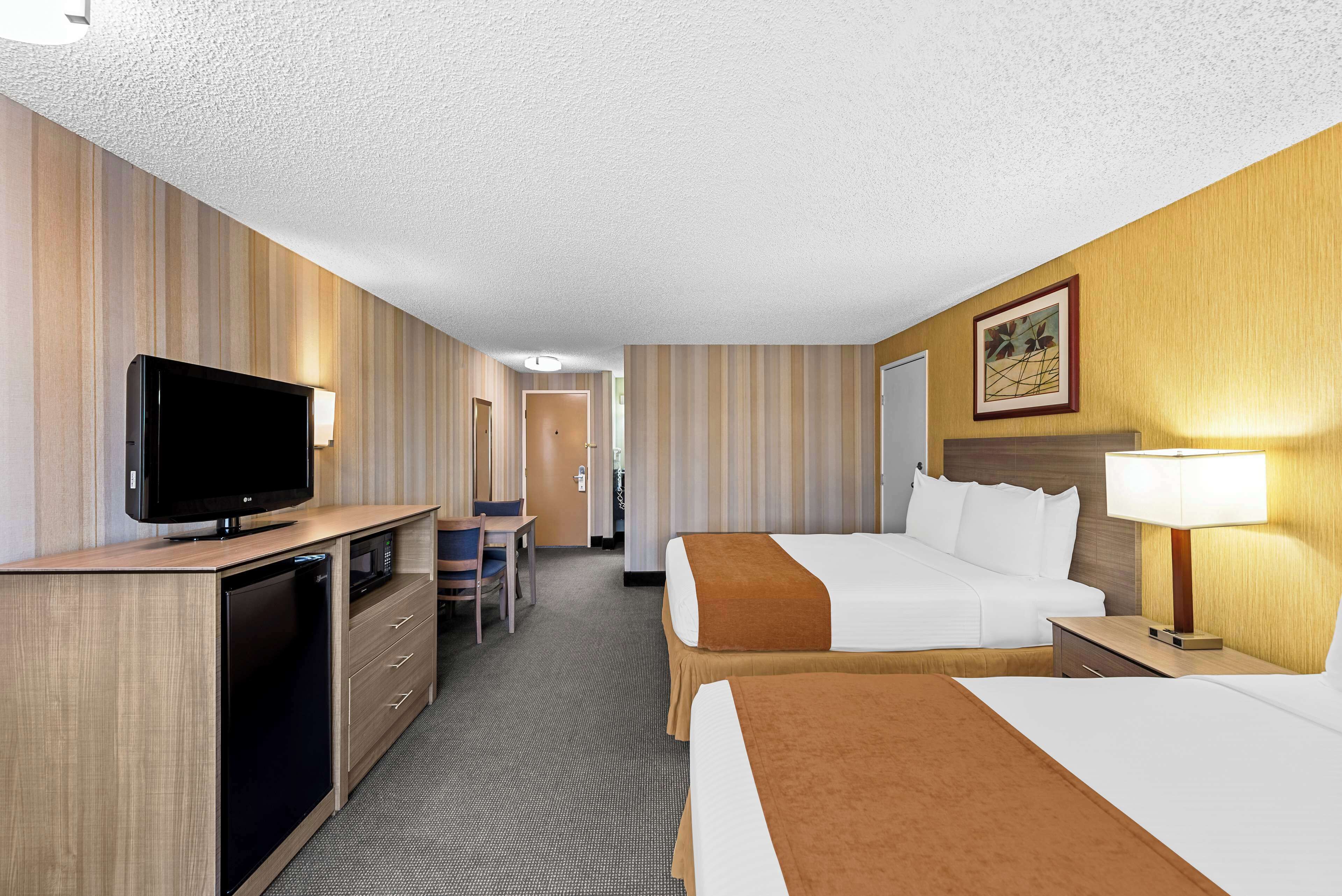 A hotel room with a television, desk, chair, two beds, and a nightstand with a lamp.