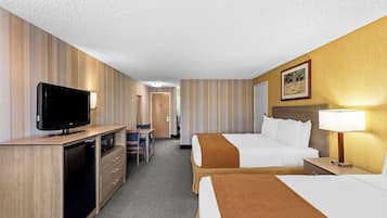 A hotel room with a television, desk, chair, two beds, and a nightstand with a lamp.