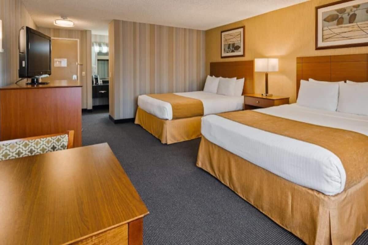 A hotel room with two beds, a desk, a television, and a dining area.