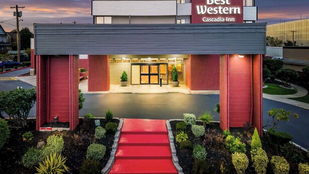 A hotel entrance with a red awning, a sign reading "Best Western Cascadia Inn," and a well-maintained garden with various shrubs and a red pathway leading to the entrance. - Best Western Cascadia Inn (Everett)
