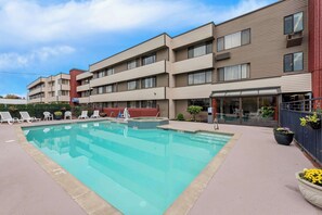 A modern hotel with a swimming pool, lounge chairs, and potted plants.
