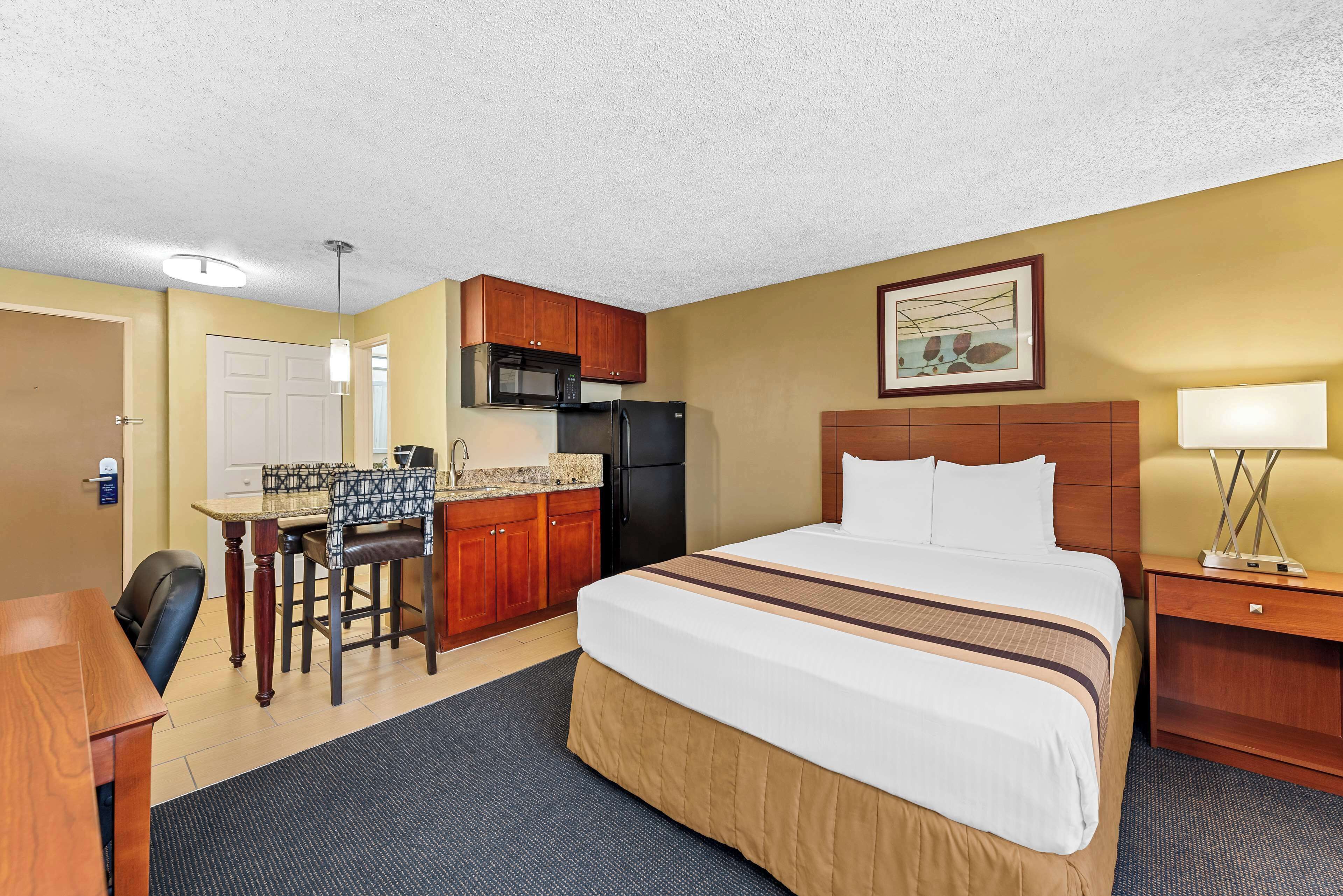A hotel room with a bed, a desk, a microwave, a refrigerator, and a dining area.