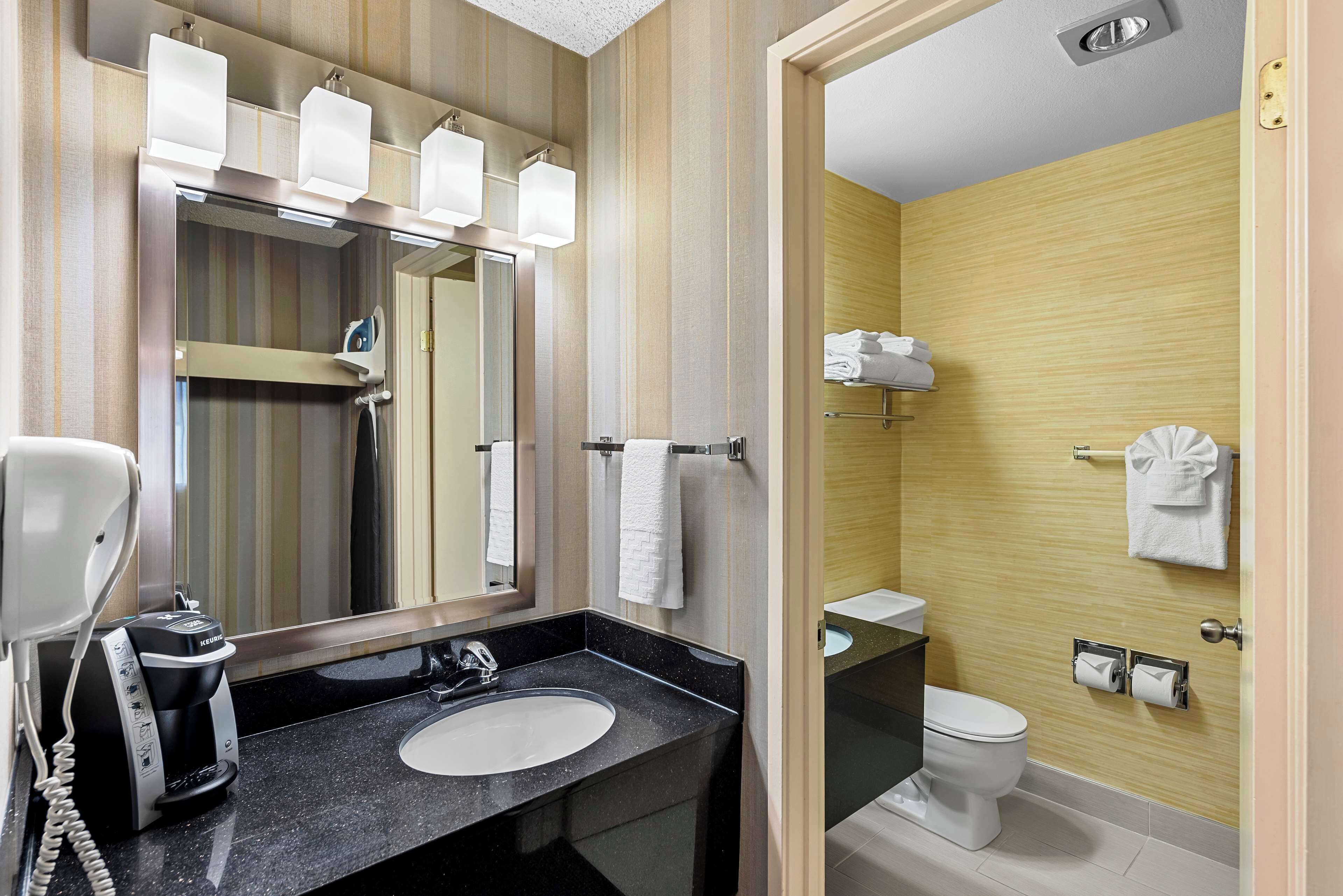 A modern bathroom with a large mirror, a black countertop sink, a built-in toilet, and a shower area.