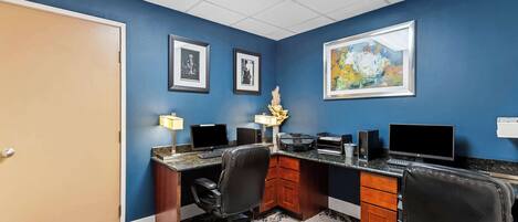 A conference room with a blue wall, a wooden desk, two chairs, a computer, and framed pictures.