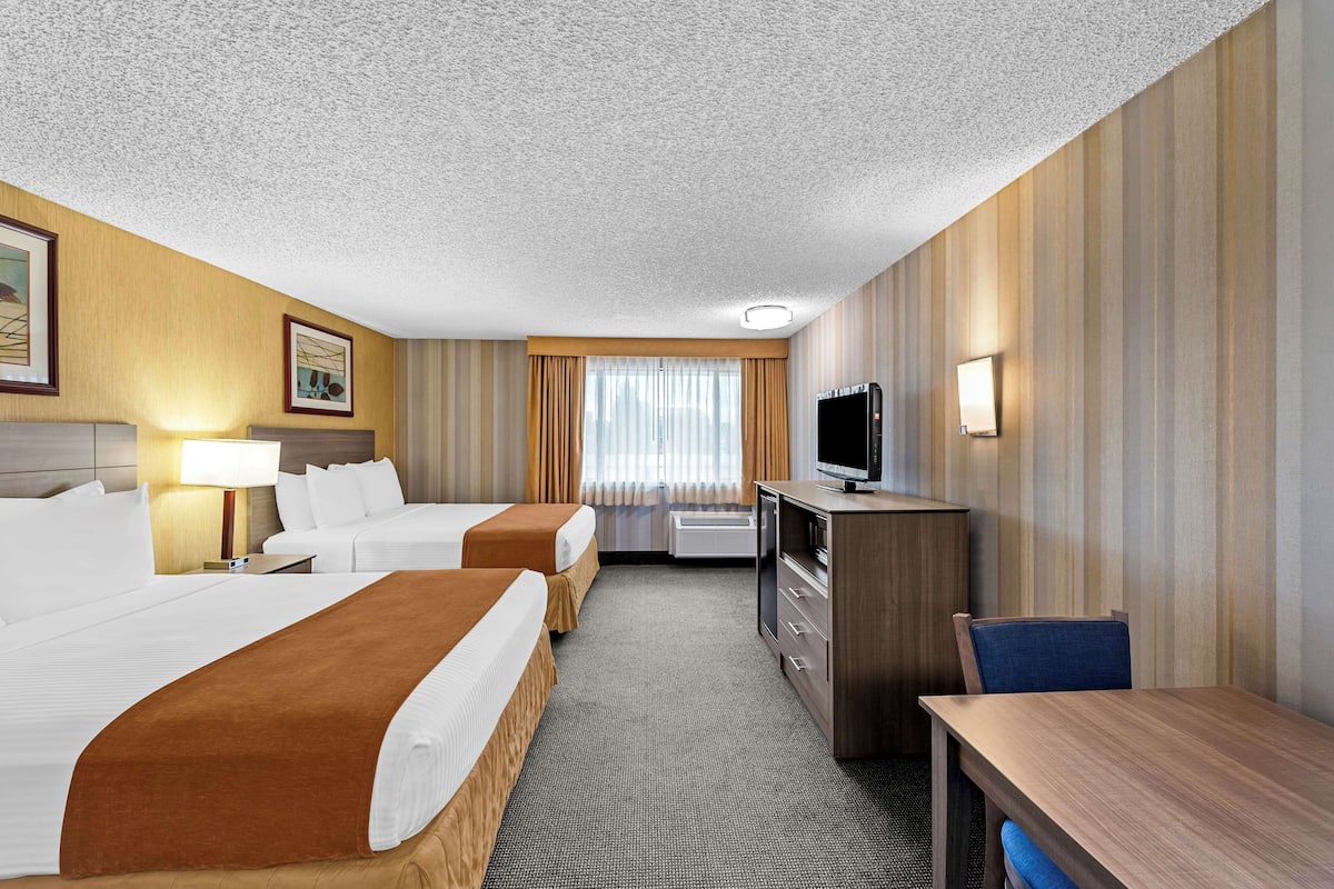 A hotel room with two beds, a desk, a TV, and a lamp.