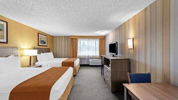 A hotel room with two beds, a desk, a TV, and a lamp.