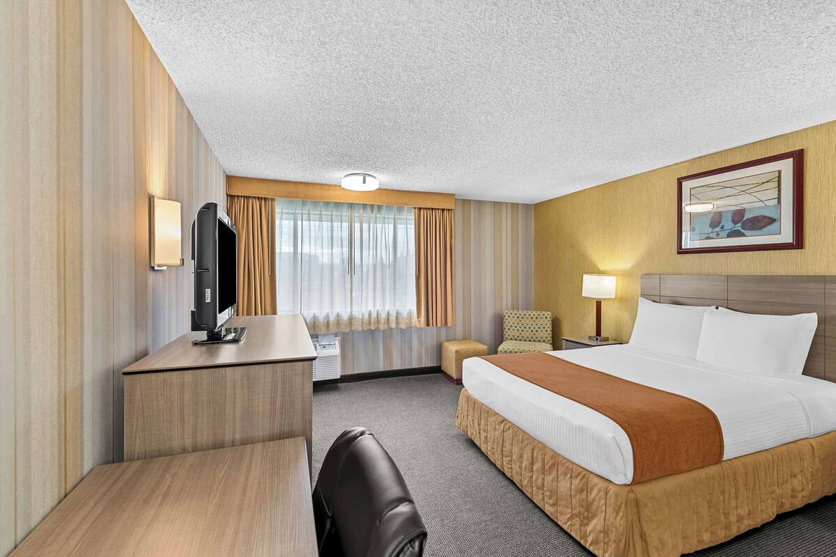 A hotel room with a bed, desk, chair, and a television.