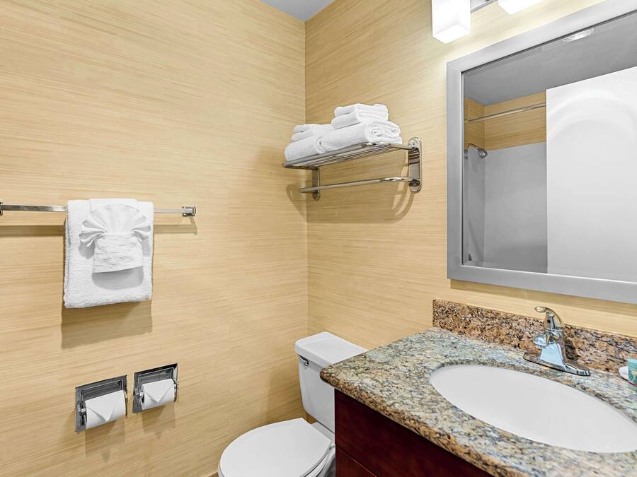 Un baño moderno con pared de madera, un lavamanos con encimera de granito, un inodoro, un perchero con toallas dobladas y un espejo.