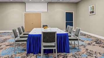Una sala de conferencias con mantel azul, sillas grises, una pantalla de proyector y piso alfombrado.