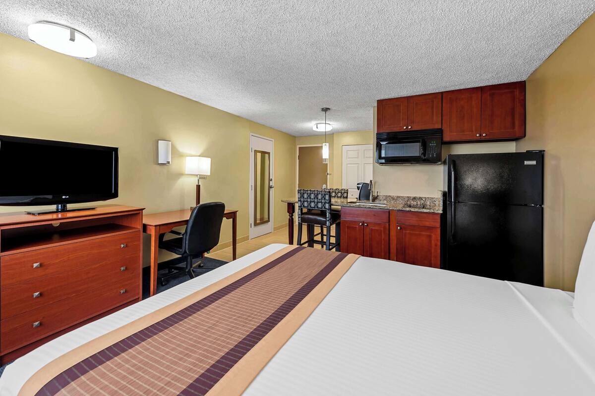 A hotel room with a bed, a desk, a television, a microwave, a refrigerator, and a kitchenette.