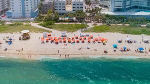 An aerial view of a beach with umbrellas and people, surrounded by buildings.