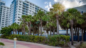 A hotel with a modern design, featuring a prominent building with balconies and a clear view of the surrounding palm trees and pathway. - Crystal Beach Suites Miami Oceanfront Hotel (Miami Beach)