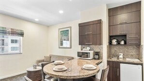 A modern kitchen with dark wood cabinets, a granite countertop, and a built-in microwave. - Crystal Beach Suites Miami Oceanfront Hotel (Miami Beach)