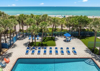 A modern kitchen with dark wooden cabinets, a built-in microwave, and a dining area with two chairs. A beige sofa is positioned near a large window with a view of the ocean. at Crystal Beach Suites Miami Oceanfront Hotel