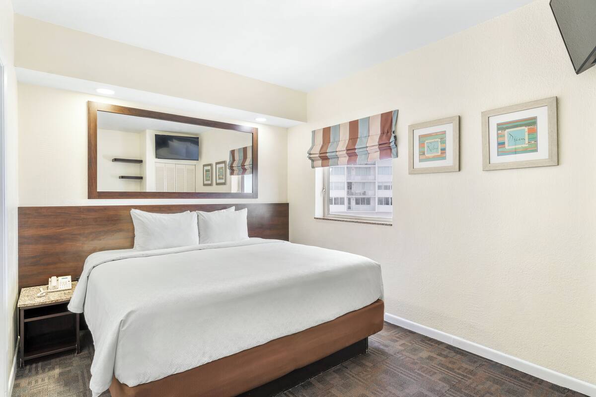 A hotel room with a large bed, a nightstand, a mirror, and two framed pictures on the wall.