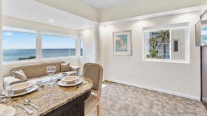 A dining area with a view of the ocean, a sofa, and a dining table set with plates and glasses.
