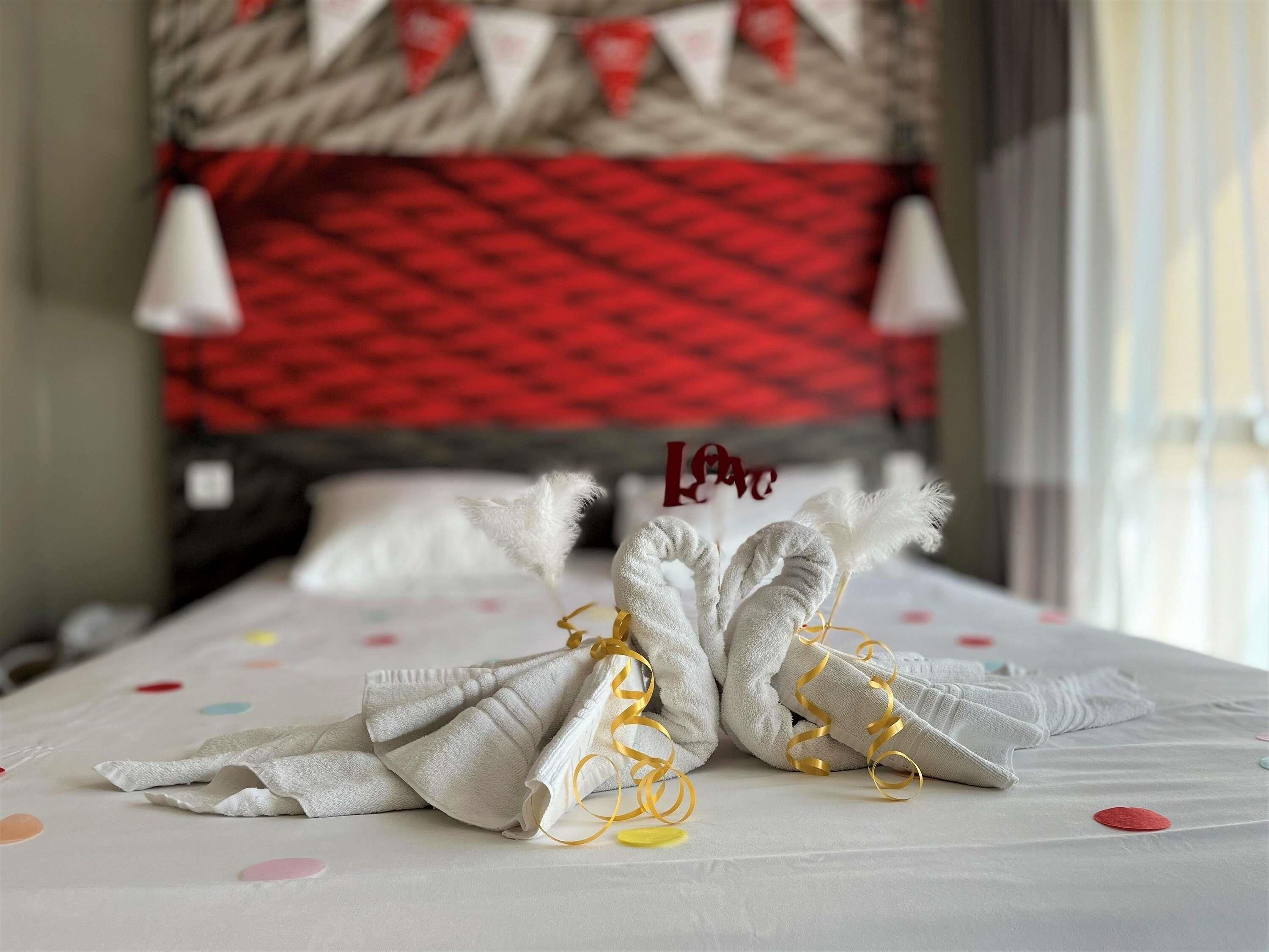 Un letto rifatto con cura, decorato con un cuscino ornamentale e un cartello con scritto 'Love', una coperta a pois e una testata beige e rossa.