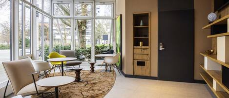 A modern interior with large windows, a wooden bookshelf, and a seating area with tables and chairs.