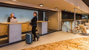 A reception desk with a laptop, a person with a suitcase, and a staircase with chairs. - ibis Heidelberg Hauptbahnhof (Heidelberg)