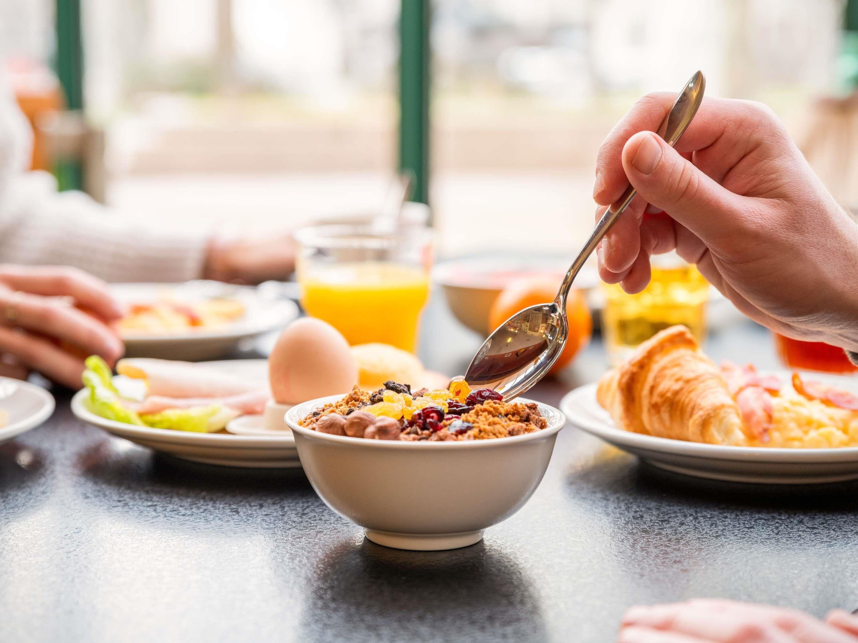 Desayuno con un tazón de cereal, un croissant y un vaso de jugo de naranja sobre una mesa.