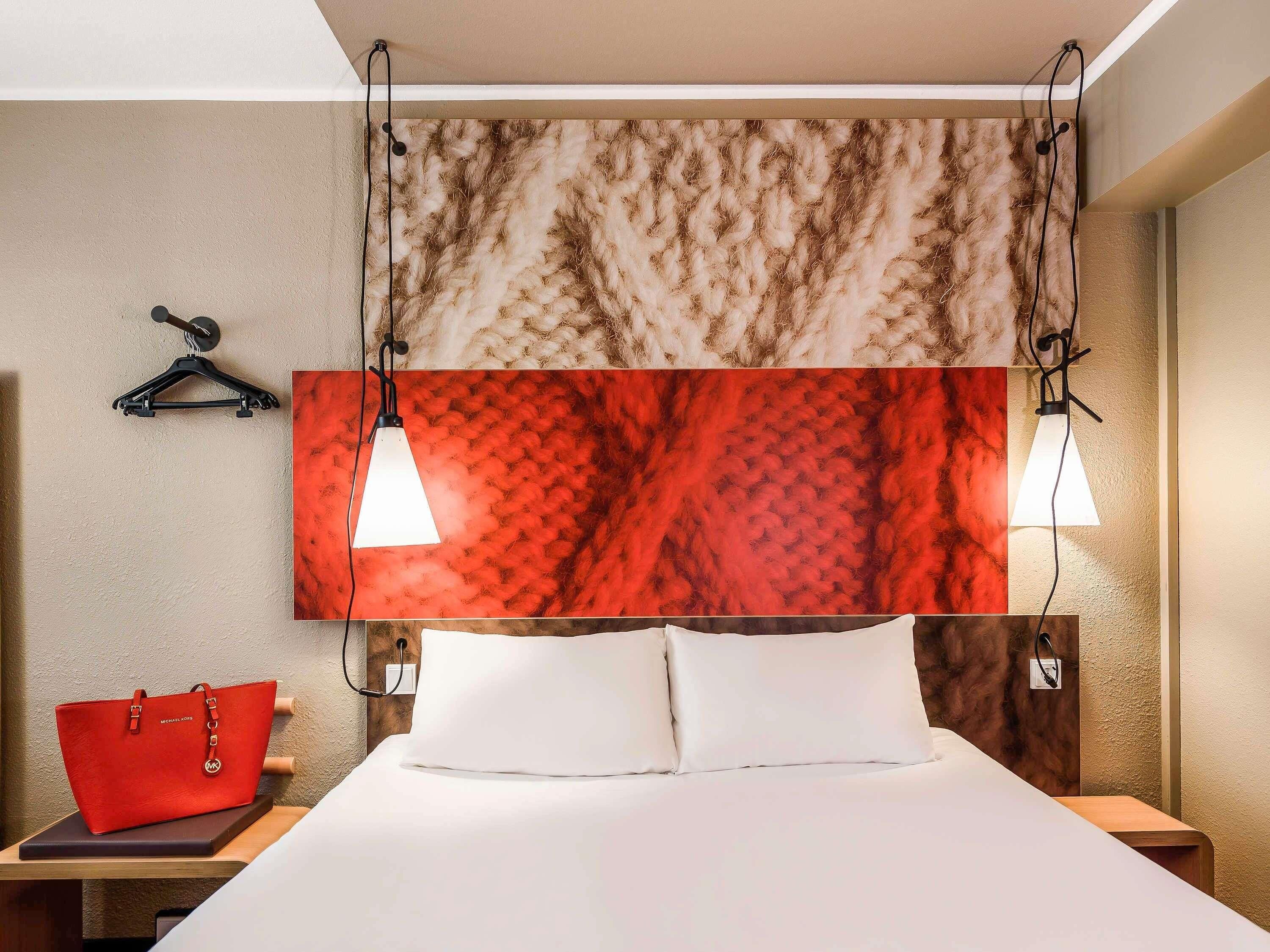 A hotel room with a bed, a red handbag, and a wall with a textured pattern.