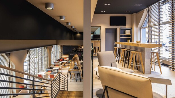 A modern interior with a staircase, seating areas, and a bar. - ibis Heidelberg Hauptbahnhof (Heidelberg)