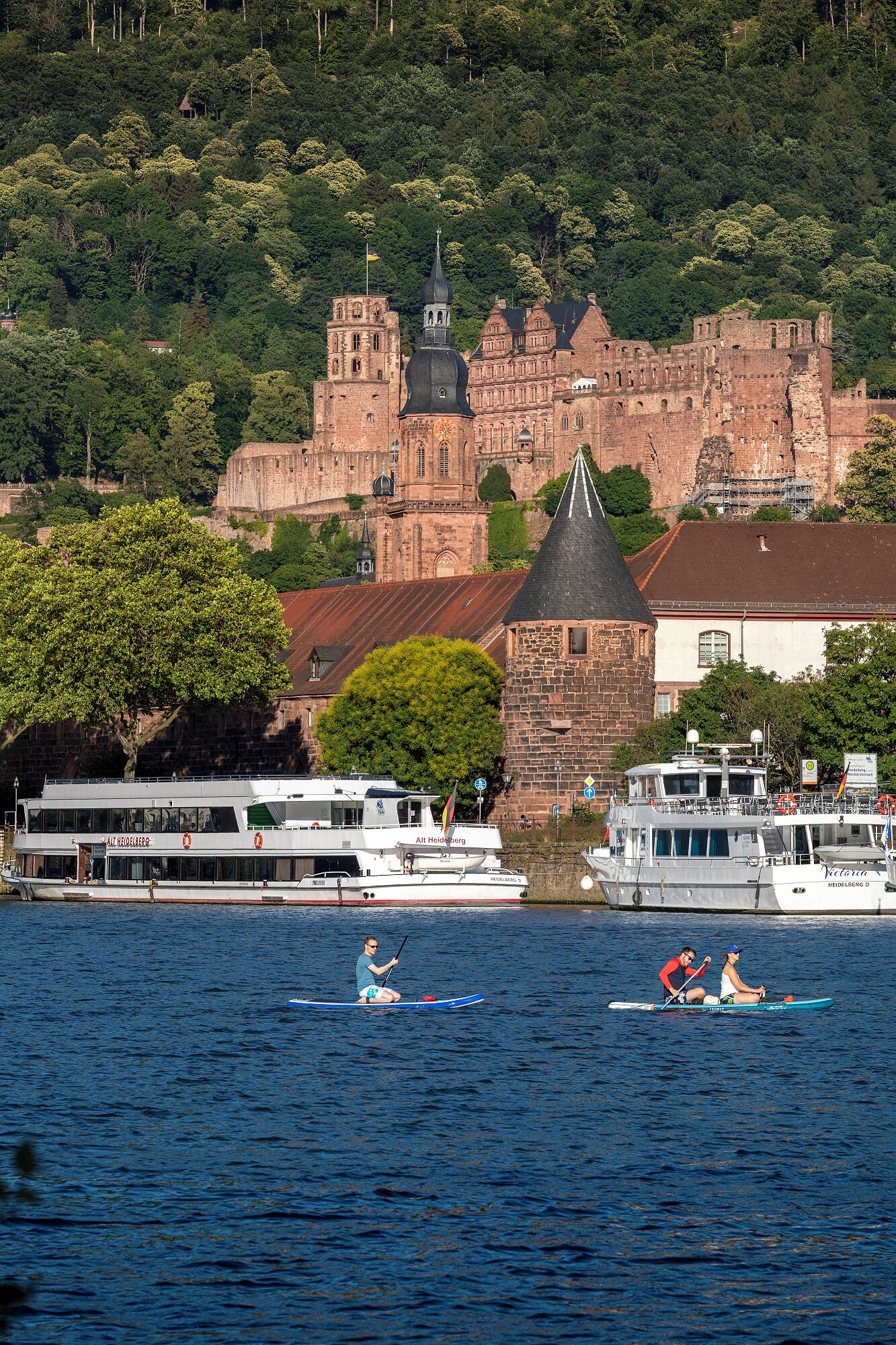 A historic castle with a prominent tower and a river in the foreground with boats.