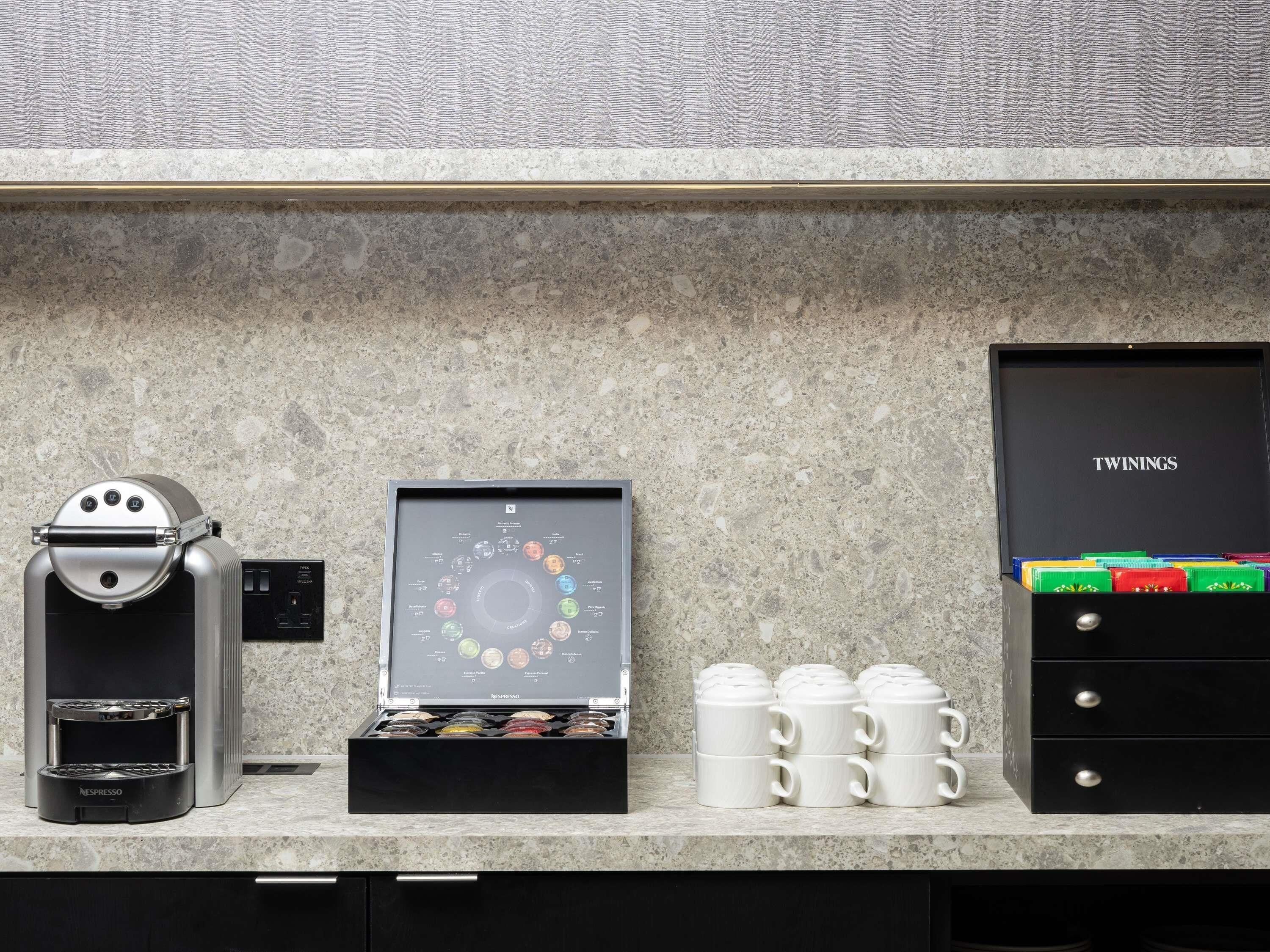 A coffee machine, a coffee pod display, and a drawer with mugs on a kitchen counter.