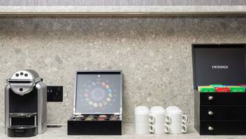 Una cafetera, un expositor de cápsulas de café y un cajón con tazas en una encimera de cocina.