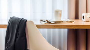A modern chair with a black jacket draped over it, a white mug, and a white device on a wooden table.
