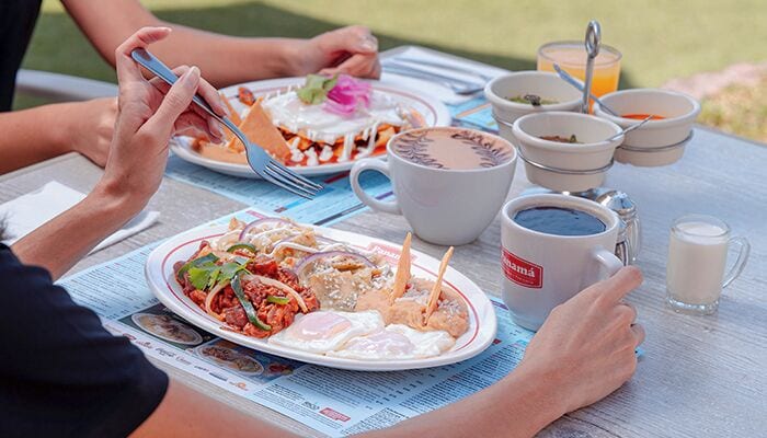 A dining table with plates of food, cups, and a newspaper.