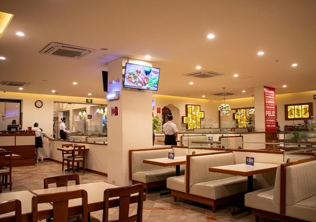 L’intérieur d’un restaurant avec des banquettes et des tables, un écran de télévision et un panneau affichant le menu.