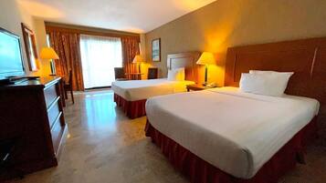 A hotel room with two beds, a desk, a TV, and a window with curtains.